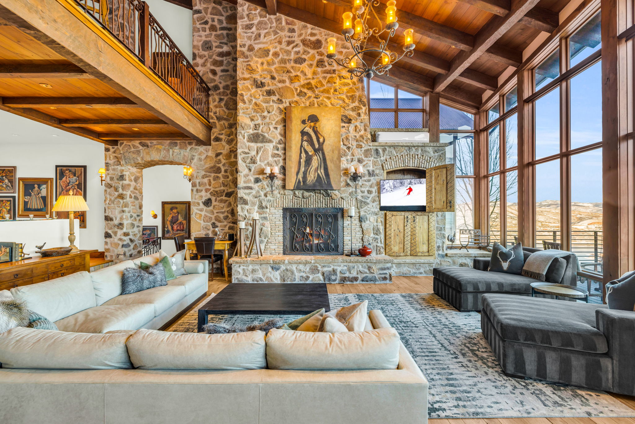 the view from the great room of Snow Pine in Park City, there is a large stone fireplace with a giant piece of artwork and a view of the mountains