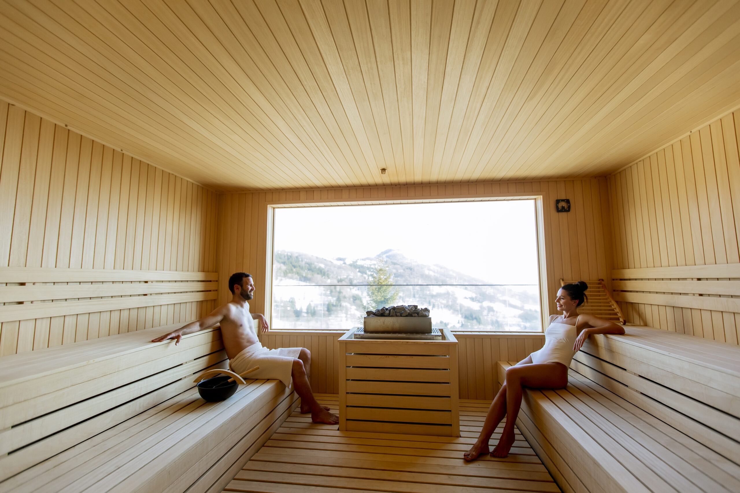 Handsome young couple relaxing in the sauna and watching winter forest through the window in Park City