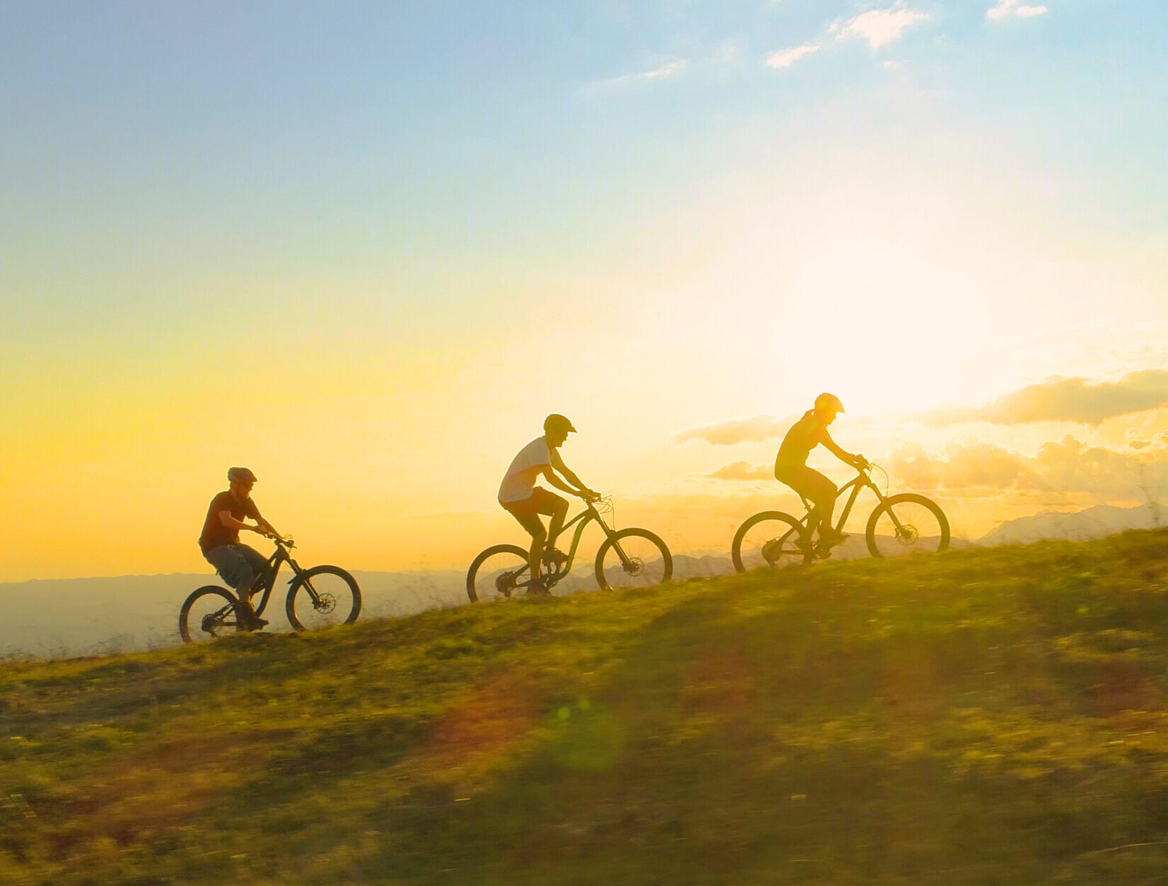 Fit tourists riding electric bicycles along a grassy path on a beautiful sunny spring day. Cinematic shot of three friends enjoying a scenic mountain bike ride in Park City Utah