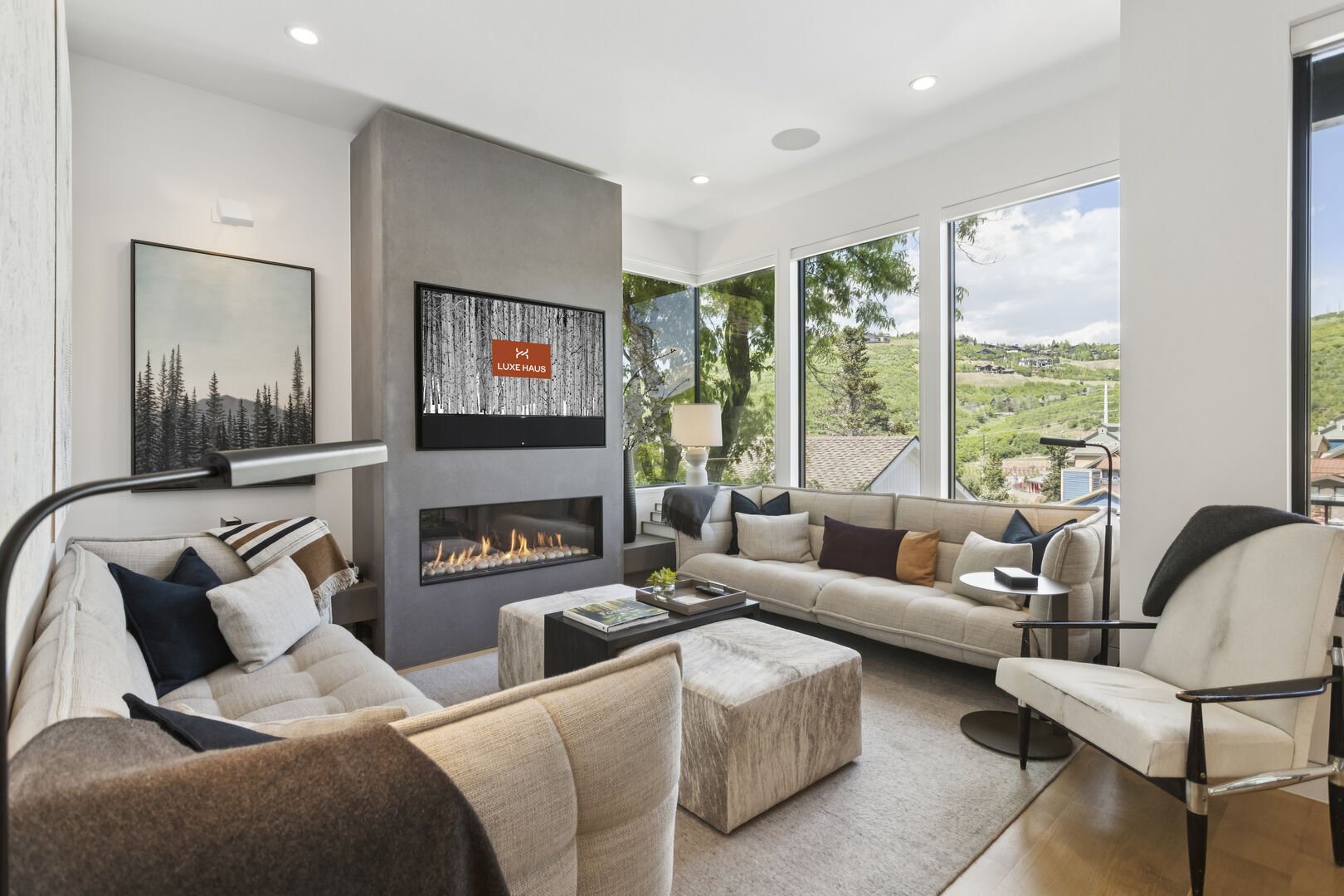 a chic living room area with a view of main street in park city, fire is burning and the screen saver has the Luxe Haus logo on the TV
