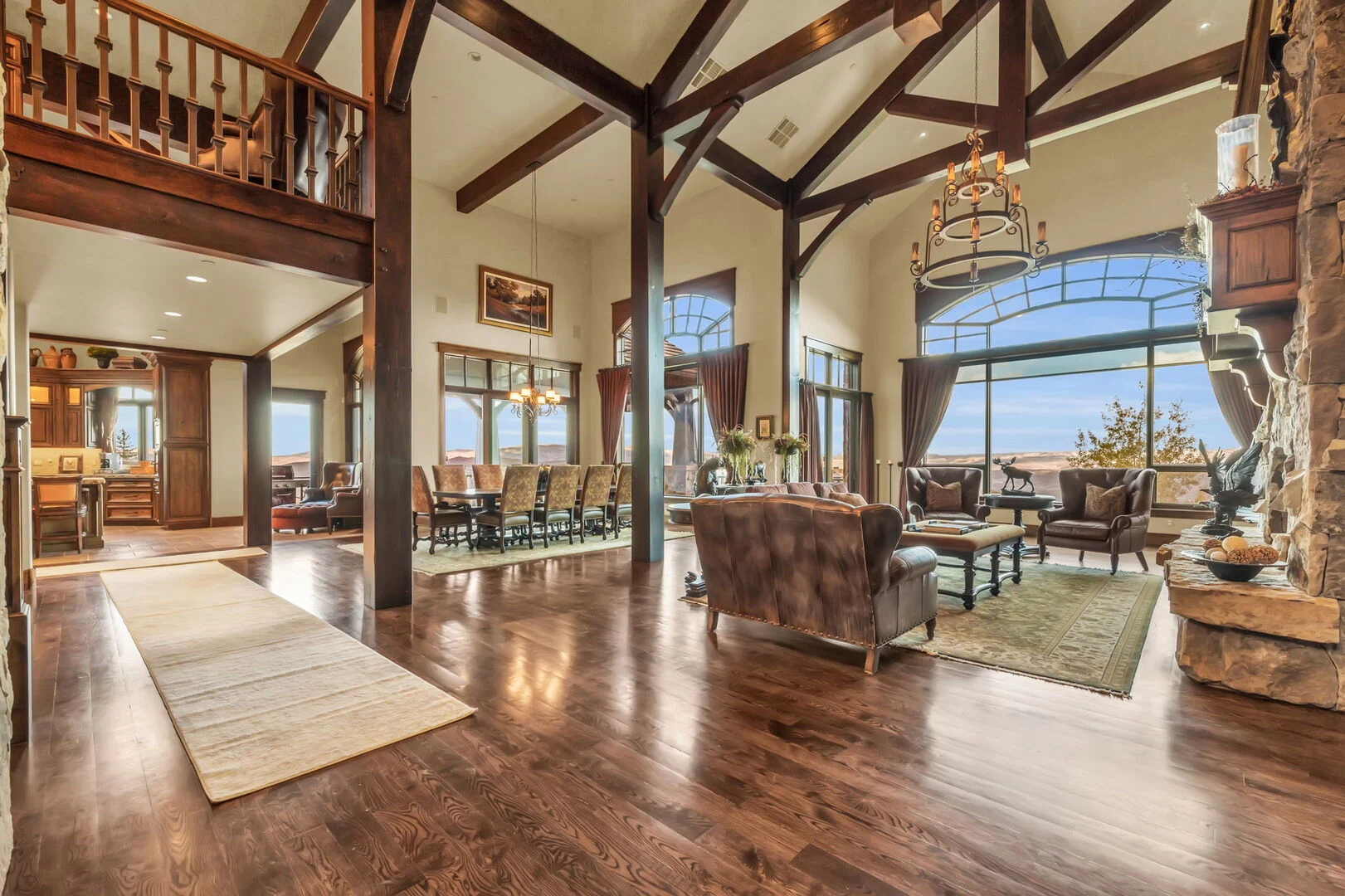 an elegant living area with large windows overlooking the mountains and lake and wood beam accents with rich colored furniture