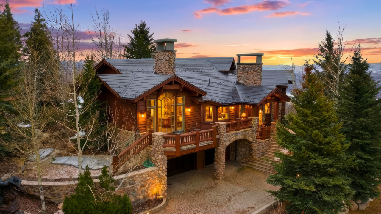 Summit View Lodge at Deer Crest at sunset. the lights are glowing from inside a stately log cabin lodge with the view of the mountains of park city in the background
