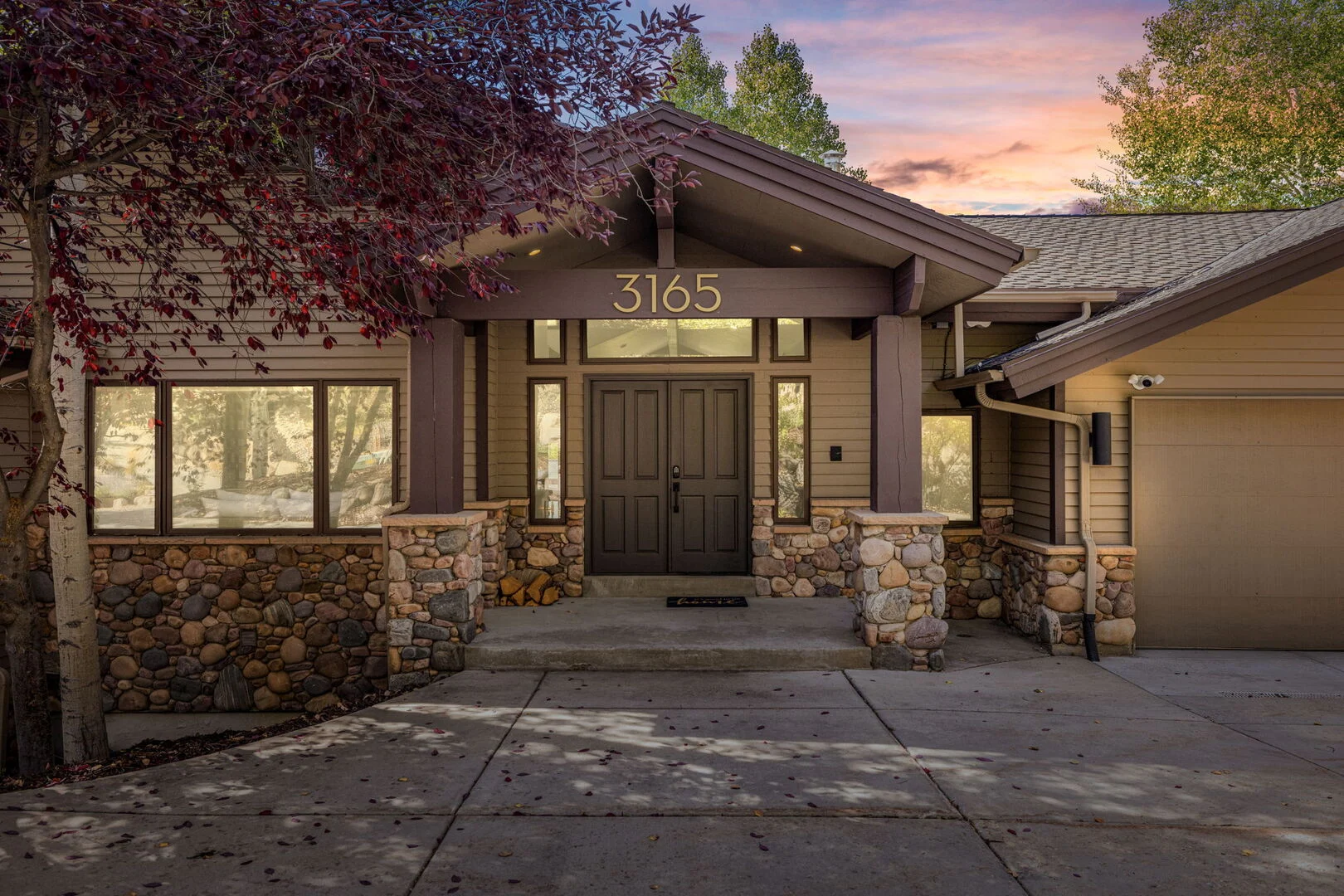 A luxury home at sunset, lights are glowing from within. there are trees around the property named Deer Valley Bliss